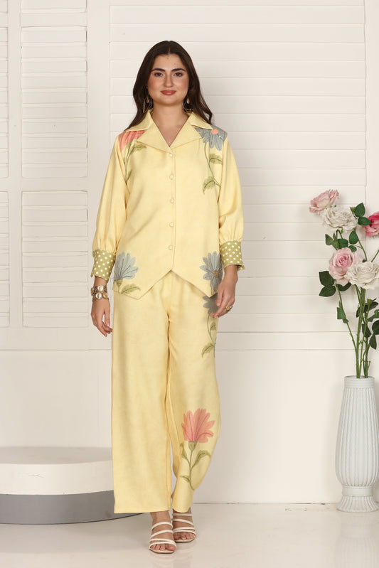 Woman in a yellow floral outfit standing on a white floor with flowers and a vase.